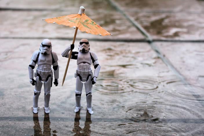 A photograph of two Stormtrooper toy figures standing in the rain with a cocktail umbrella held above them both