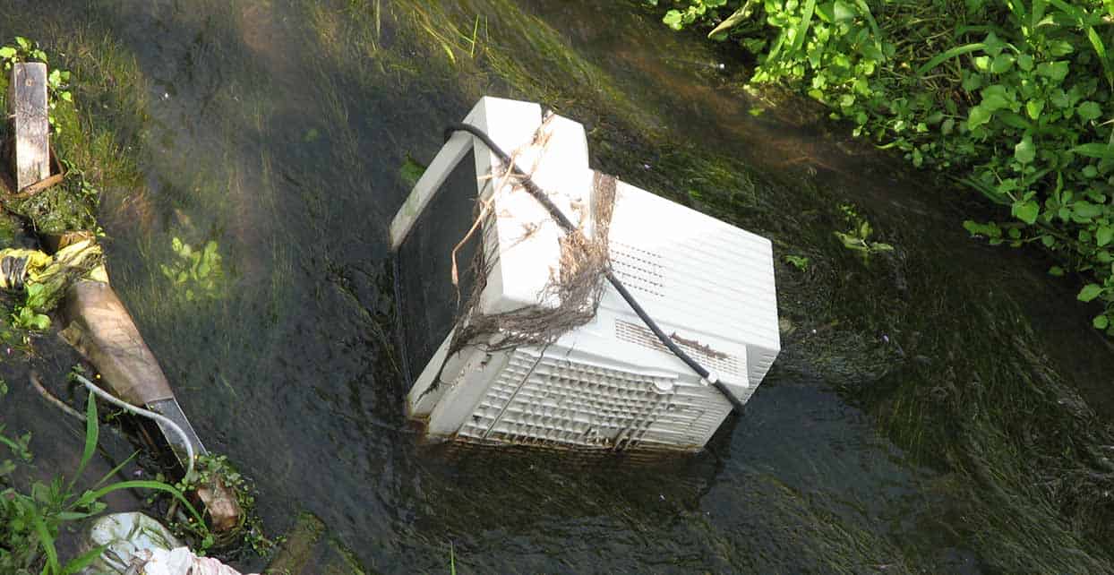Photograph of a broken CRT monitor sitting in a river.