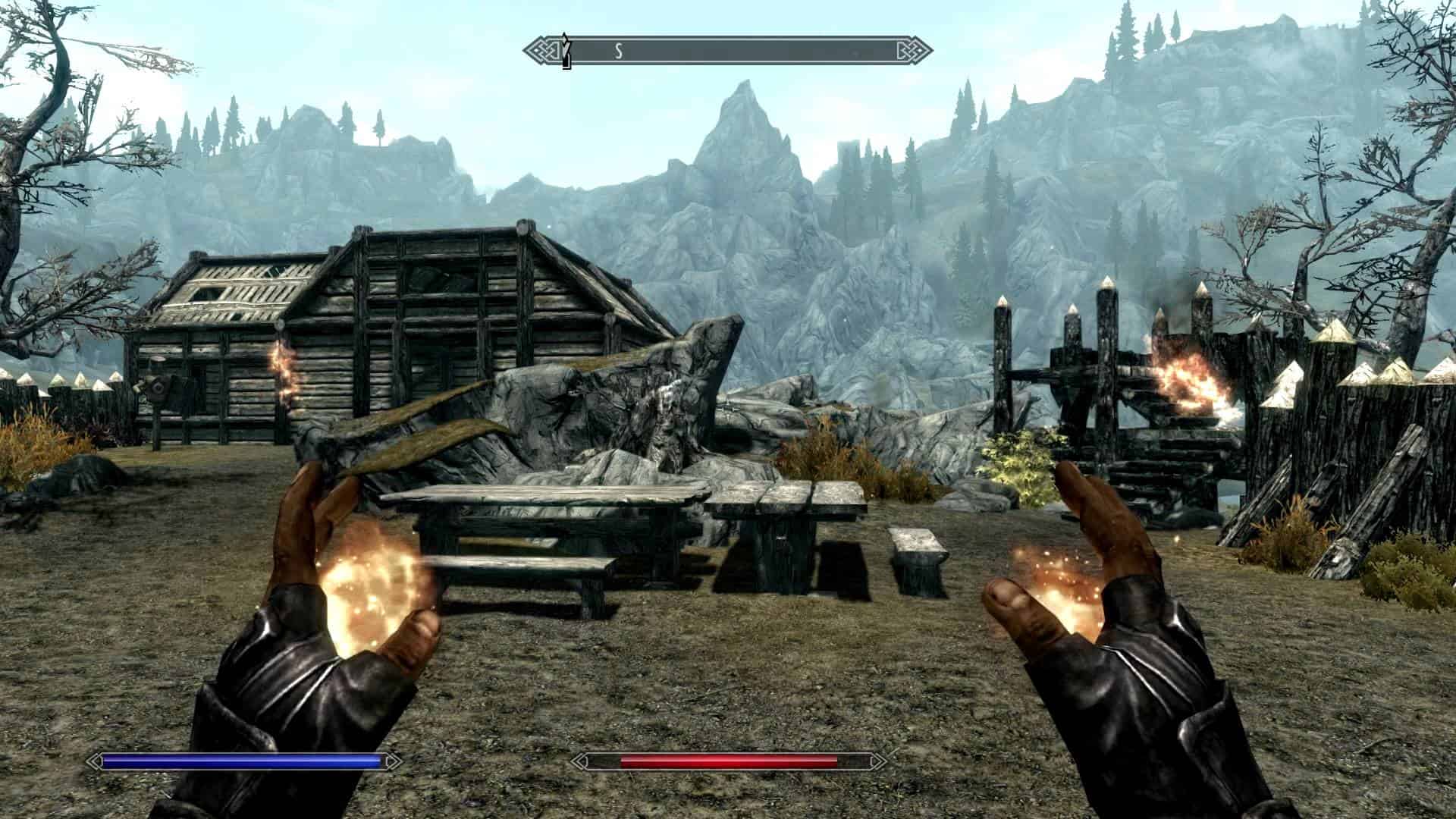 Screenshot from the game Skyrim. The player is facing some mountains and a wooden shed wielding a fireball spell in their hands.
